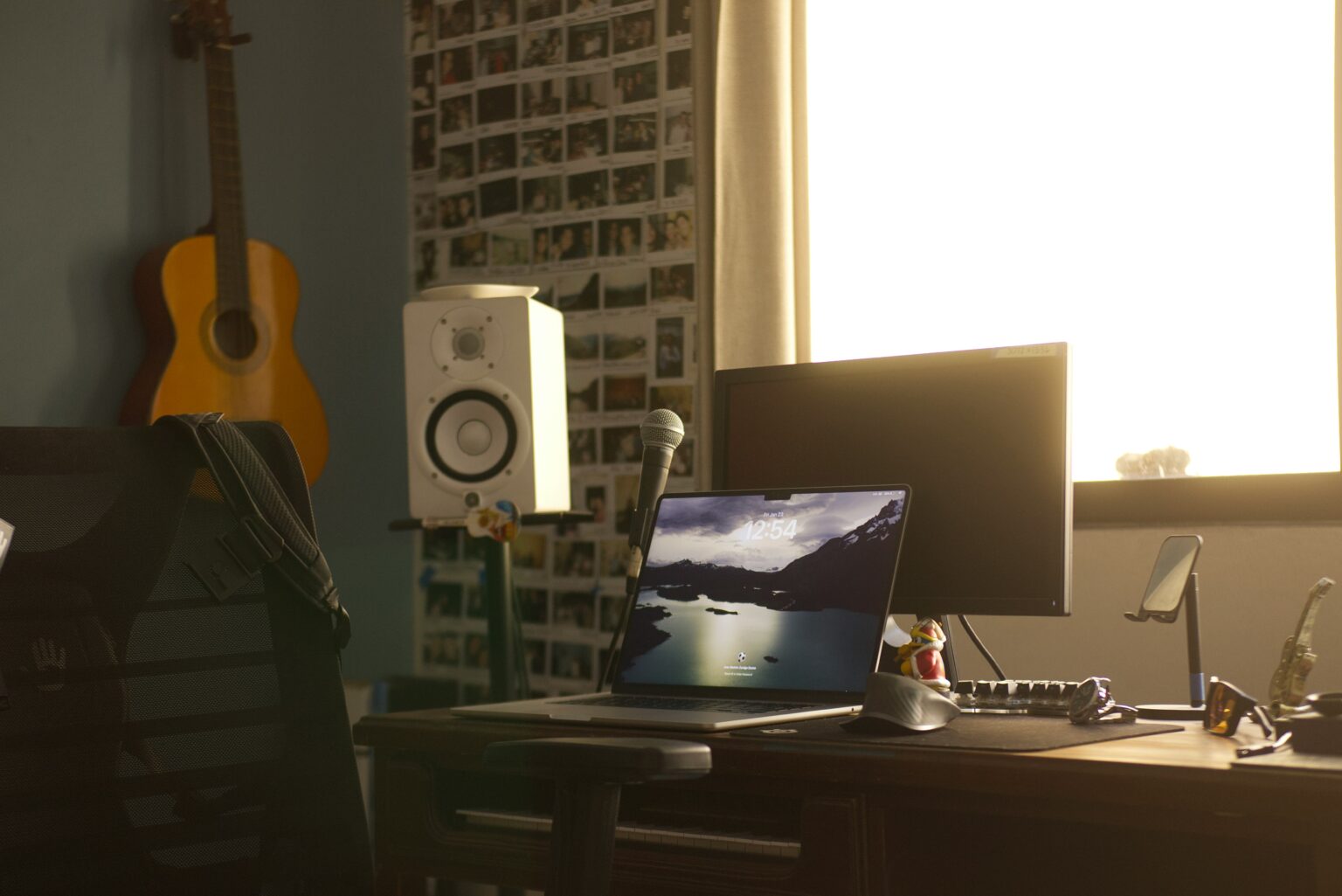 Bureau home-studio avec ordinateur portable, ecran, micro et guitare accrochee au mur