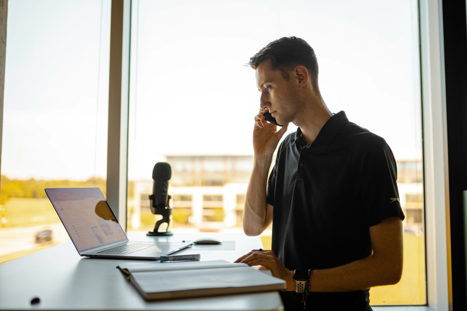 Un homme au telephone pres de son ordinateur portable, dans un bureau lumineux